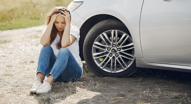 woman sitting in front of her broken car